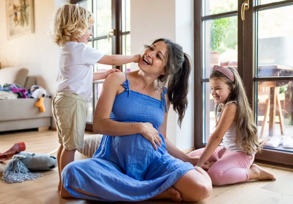 Pregnant mother with children indoors, laughing together.