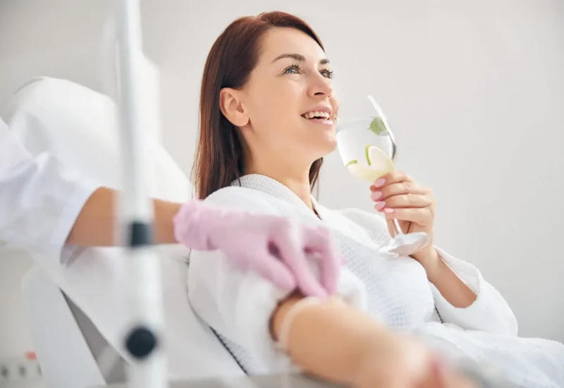 Joyous female patient drinking a healthy beverage during a medical procedure in a beauty clinic