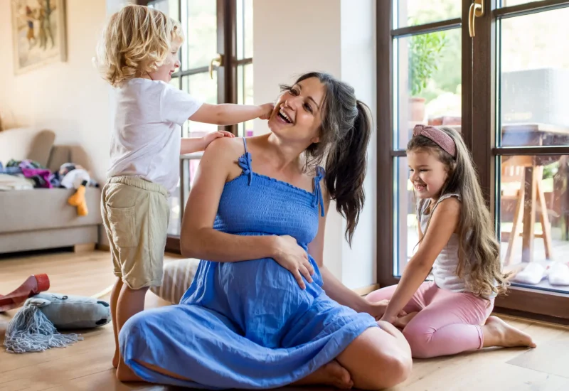 Pregnant mother with children indoors, laughing together.
