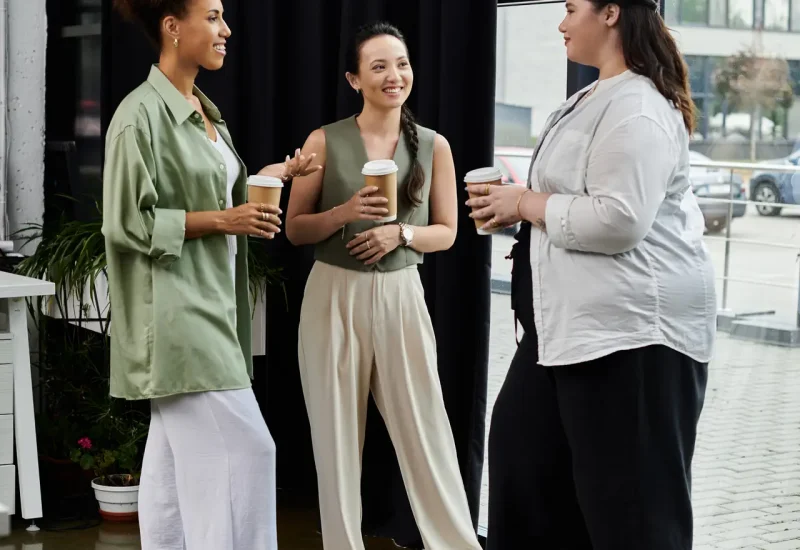 Three stylish professionals engage in lively conversation while sipping coffee in the office.